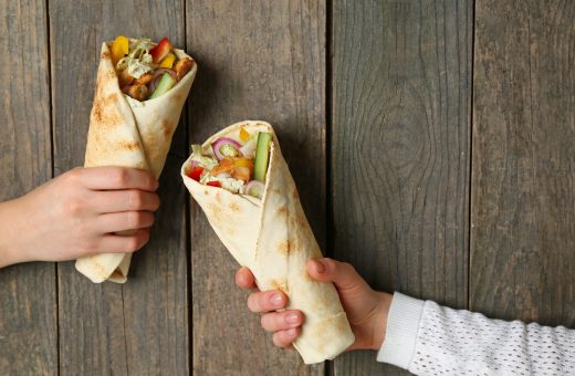 female hands with tasty doner kebab on wooden background